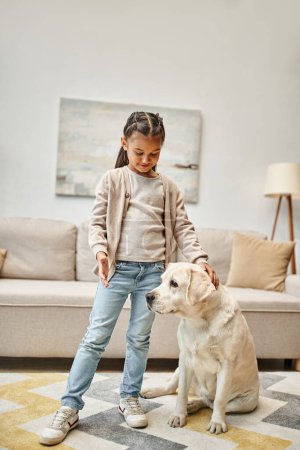 cute girl in casual wear training labrador in modern living room, positive reinforcement concept