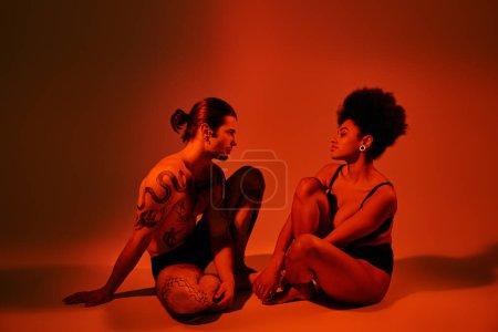 attraktive afrikanisch-amerikanische Frau schaut ihren tätowierten Freund an, während beide auf dem Boden sitzen