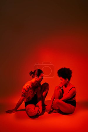 Photo for Beautiful african american woman looking at her tattooed boyfriend while both sitting on floor - Royalty Free Image