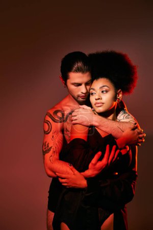 Téléchargez les photos : Bel homme tatoué embrassant amoureusement sa petite amie afro-américaine par derrière, couple sexy - en image libre de droit