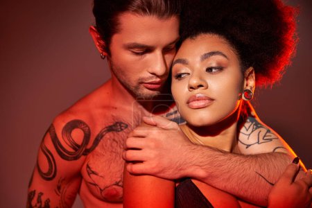 Téléchargez les photos : Beau tatouage homme étreignant chaudement sa copine afro-américaine par derrière, couple sexy - en image libre de droit