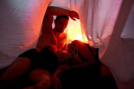 sexy diverses Paar in Unterwäsche liegt sinnlich zusammen unter Bettlaken umgeben von Lichtern
