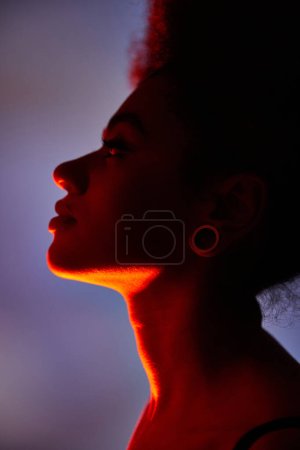 atractiva joven afroamericana con pendiente posando en perfil rodeado de vibrantes luces