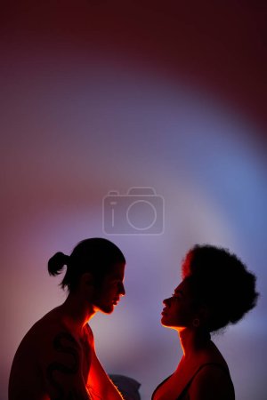 alluring sexy multicultural couple looking at each other sensually on gray background with lights