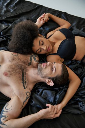Téléchargez les photos : Vue du haut de la femme afro-américaine couchée au lit à côté de son petit ami tatoué, couple sexy - en image libre de droit