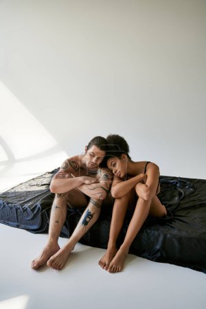 Foto de Bien parecido joven pareja multirracial en ropa interior sentado uno al lado del otro en la cama, juntos - Imagen libre de derechos