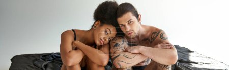 Téléchargez les photos : Attrayant jeune couple multiracial en sous-vêtements assis près de l'autre sur le lit, bannière - en image libre de droit
