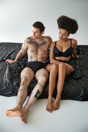 Téléchargez les photos : Multiculturel beau couple en sous-vêtements assis près de l'autre sur le lit, ensemble - en image libre de droit