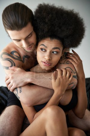 Téléchargez les photos : Jeune couple multiculturel attrayant en sous-vêtements assis sur leur lit et étreignant avec amour - en image libre de droit