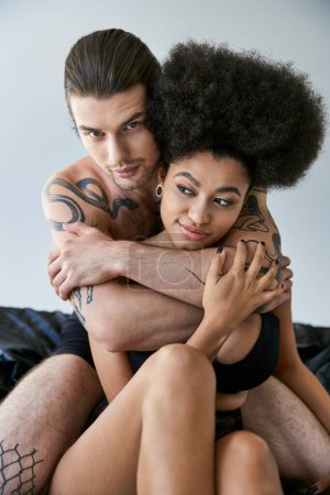 Téléchargez les photos : Sexy interracial couple en sous-vêtements assis sur leur lit et étreignant amoureusement, ensemble - en image libre de droit