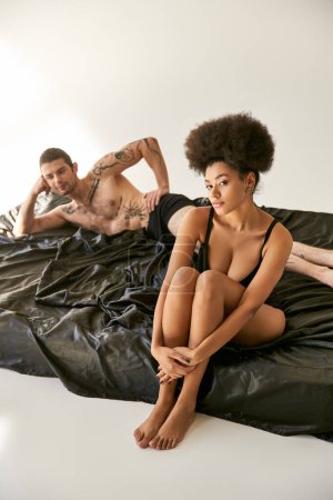 Foto de Se centran en la mujer afroamericana en lencería sexy sentada junto a su novio borroso, pareja sexy - Imagen libre de derechos
