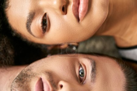 close up view of attractive sexy multicultural couple lying and looking straight at camera