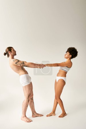 Photo for Beautiful multiracial sexy couple in underwear holding hands and looking at each other sensually - Royalty Free Image