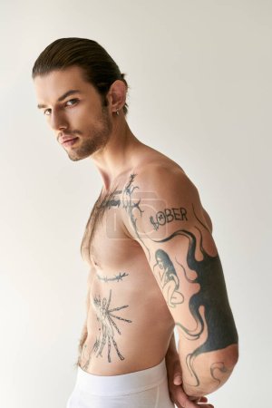 tempting man with ponytail and stylish tattoos in comfy underwear posing on ecru background