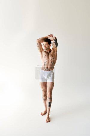 Foto de Sexy atractivo hombre con cola de caballo y fresco tatuajes en ropa interior cómoda posando sobre fondo crudo - Imagen libre de derechos