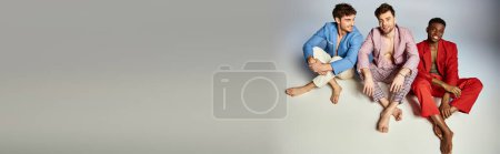 Photo for Joyful multicultural friends in vibrant colorful suits sitting on floor with crossed legs, fashion - Royalty Free Image