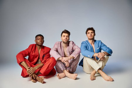 appealing diverse men in vibrant trendy suits sitting on floor with crossed legs, fashion concept