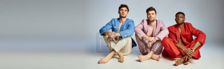 Photo for Three handsome diverse men in vibrant trendy suits sitting on floor with crossed legs, banner - Royalty Free Image