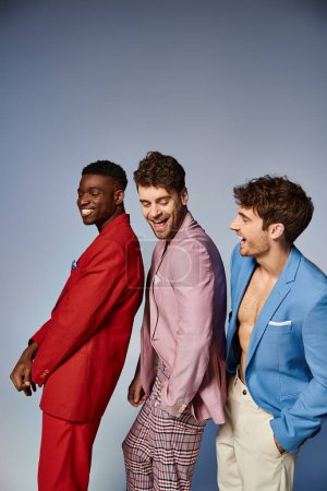 joyous handsome diverse men in stylish vibrant suits posing in single file on gray backdrop