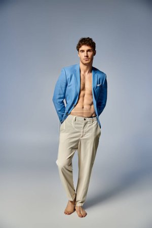 jeune homme attrayant en veste bleue déboutonnée vibrante posant sur fond gris, concept de mode