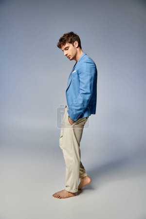 jeune homme beau en veste bleue déboutonnée vibrante posant sur fond gris, concept de mode