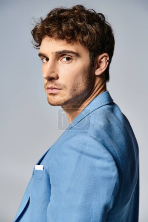 joven hombre guapo en vibrante chaqueta azul desabotonada posando sobre fondo gris, concepto de moda
