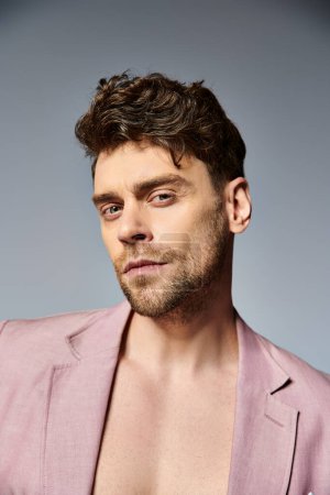 hombre de moda guapo en traje rosa vívido desabotonado posando seductor sobre fondo gris, moda