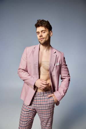 good looking man in unbuttoned vivid pink suit posing alluringly on gray backdrop, fashion concept