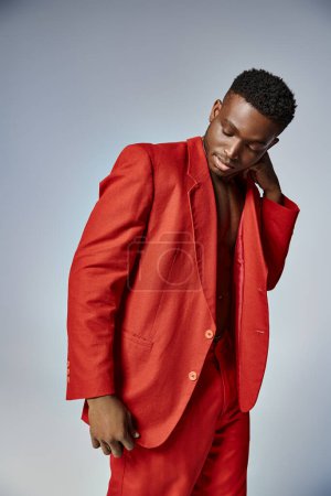 Foto de Atractivo hombre afroamericano en traje rojo vibrante posando sobre fondo gris, concepto de moda - Imagen libre de derechos