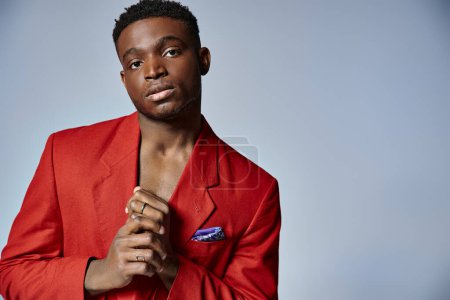 good looking young african american man in stylish red suit posing on gray backdrop, fashion concept