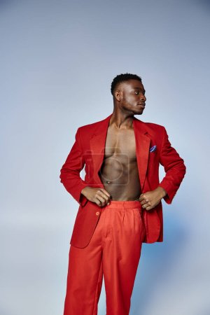 Foto de Guapo hombre afroamericano con estilo en traje rojo posando sobre fondo gris, concepto de moda - Imagen libre de derechos