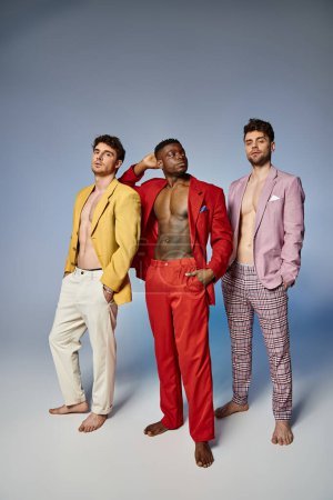 attractive multiracial friends in unbuttoned bright suits on gray background, fashion concept