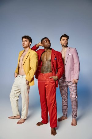 appealing sexy diverse men in unbuttoned vibrant suits posing on gray backdrop, fashion concept
