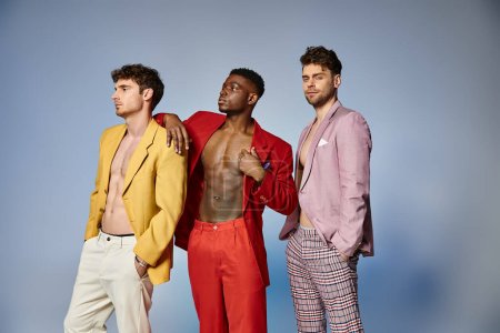 appealing multiracial friends in unbuttoned bright suits on gray background, fashion concept