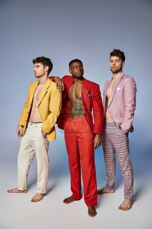 good looking multiracial friends in unbuttoned bright suits on gray background, fashion concept