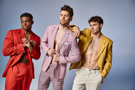 alluring sexy diverse men in unbuttoned vibrant suits posing on gray backdrop, fashion concept