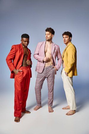 handsome multiracial friends in unbuttoned bright suits on gray background, fashion concept