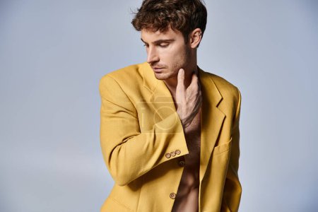attraktiver junger Mann in stylischer gelber Jacke posiert attraktiv vor grauem Hintergrund, Modekonzept