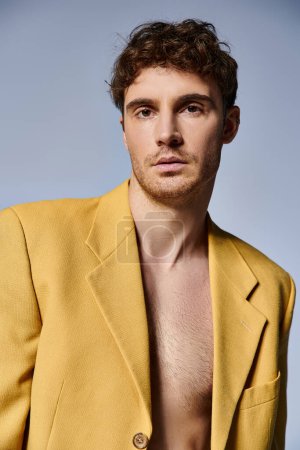atractivo joven en chaqueta amarilla de moda posando atractivamente sobre fondo gris, concepto de moda