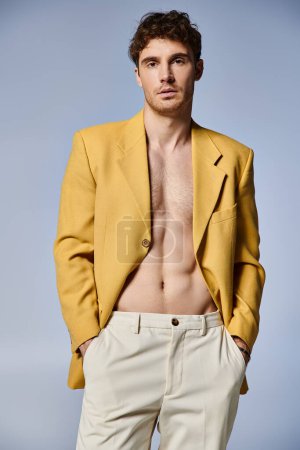joven guapo en elegante chaqueta amarilla posando atractivamente sobre fondo gris, concepto de moda