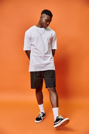 Foto de Atractivo joven afroamericano hombre en traje casual de calle sobre fondo naranja, concepto de moda - Imagen libre de derechos
