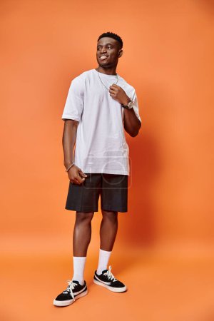 cheerful young african american man in street casual outfit on orange backdrop, fashion concept