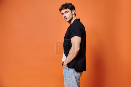 appealing stylish man in casual outfit on orange backdrop looking at camera, fashion concept