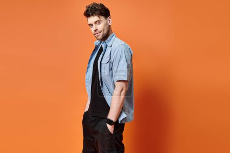 cheerful attractive man in casual outfit on orange backdrop looking at camera, fashion concept