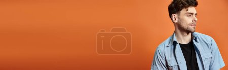 attraktiver Mann im lässigen, trendigen Outfit auf orangefarbenem Hintergrund mit Blick in die Kamera, Modekonzept
