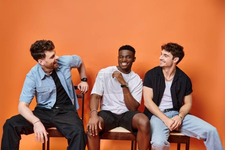 jolly diverse men in casual street outfits smiling happily on orange backdrop, fashion concept