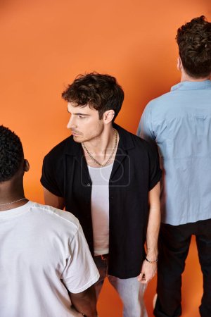 focus on young man in urban attire looking at camera with back view of his diverse friends, fashion