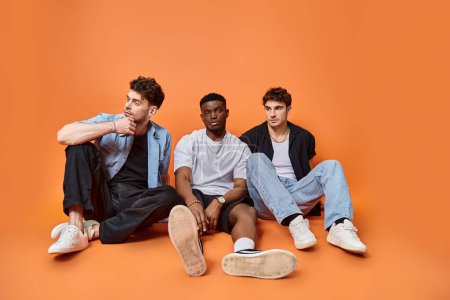 handsome multicultural stylish men in trendy urban outfits sitting on floor, fashion concept