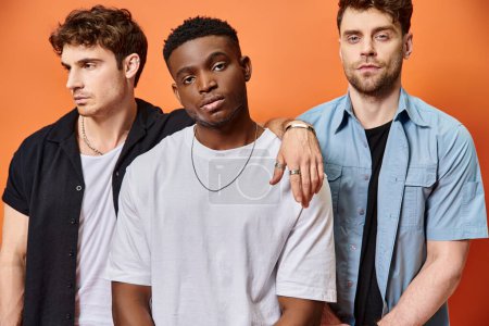 good looking multiracial male models in street attires looking at camera on orange backdrop, fashion