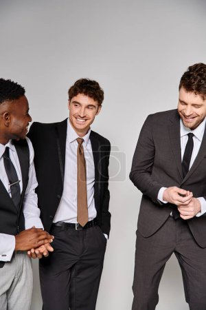attraktive, gut gelaunte Freunde in Business-Outfits, die vor grauem Hintergrund glücklich lächeln